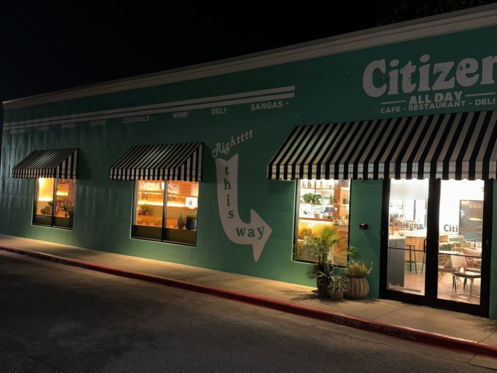 Long teal street wall with a painted menu band, three striped awnings and a white this-way arrow