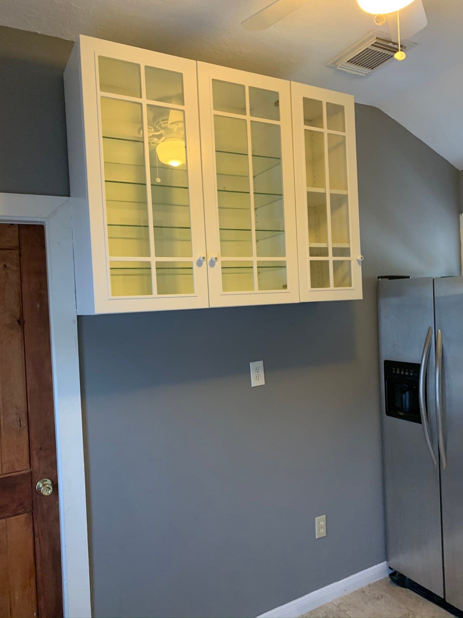 White glass-front cabinets with mullions mounted beside the refrigerator