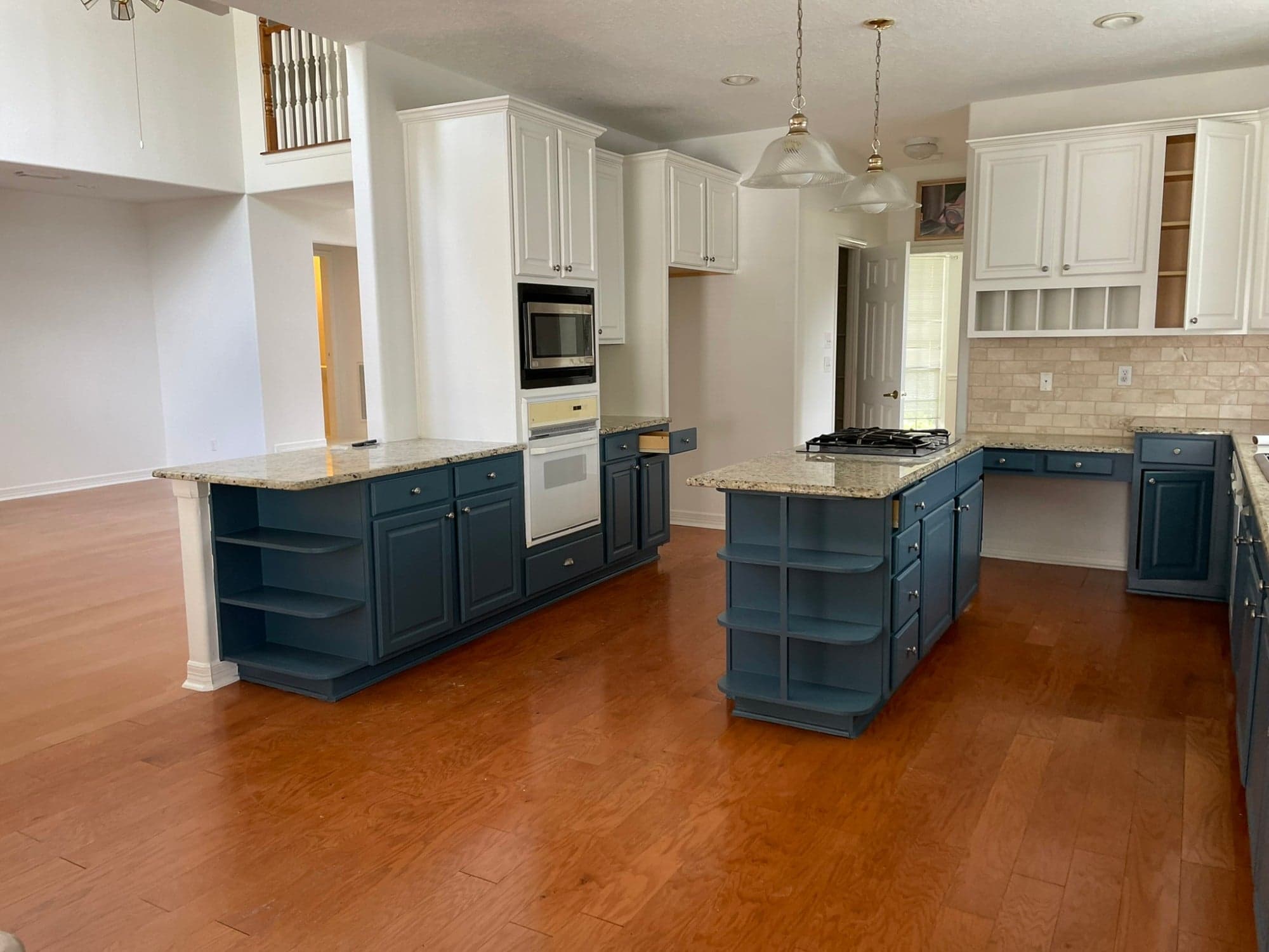 Blue painted peninsula with open end shelves, a blue island and white painted upper cabinets around a wall oven