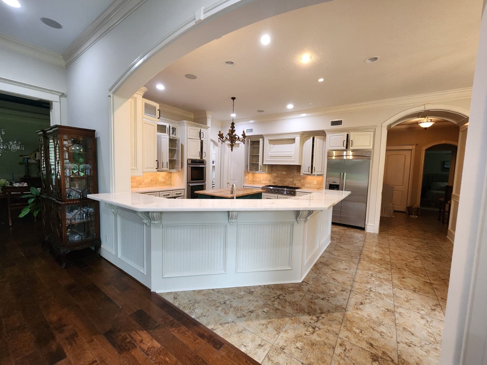 Cypress kitchen seen through an arch: white raised-panel cabinets, beadboard bar panels and a teal island