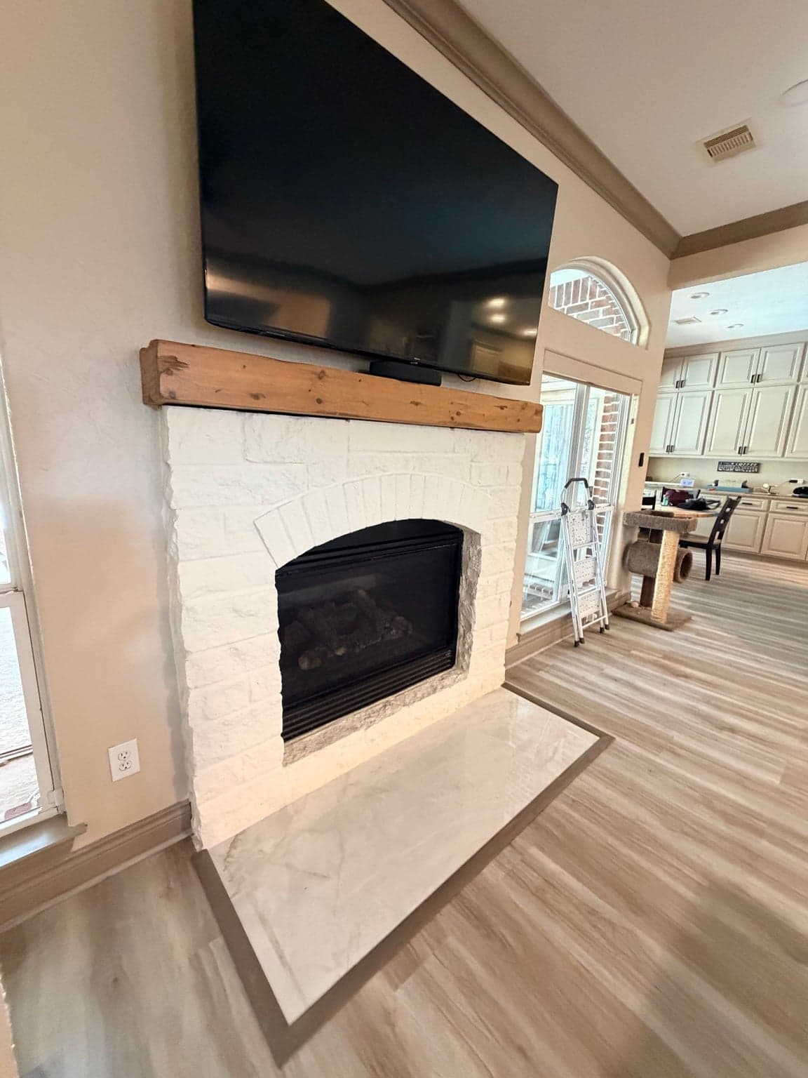 White stone fireplace with a wood mantel beside taupe baseboards
