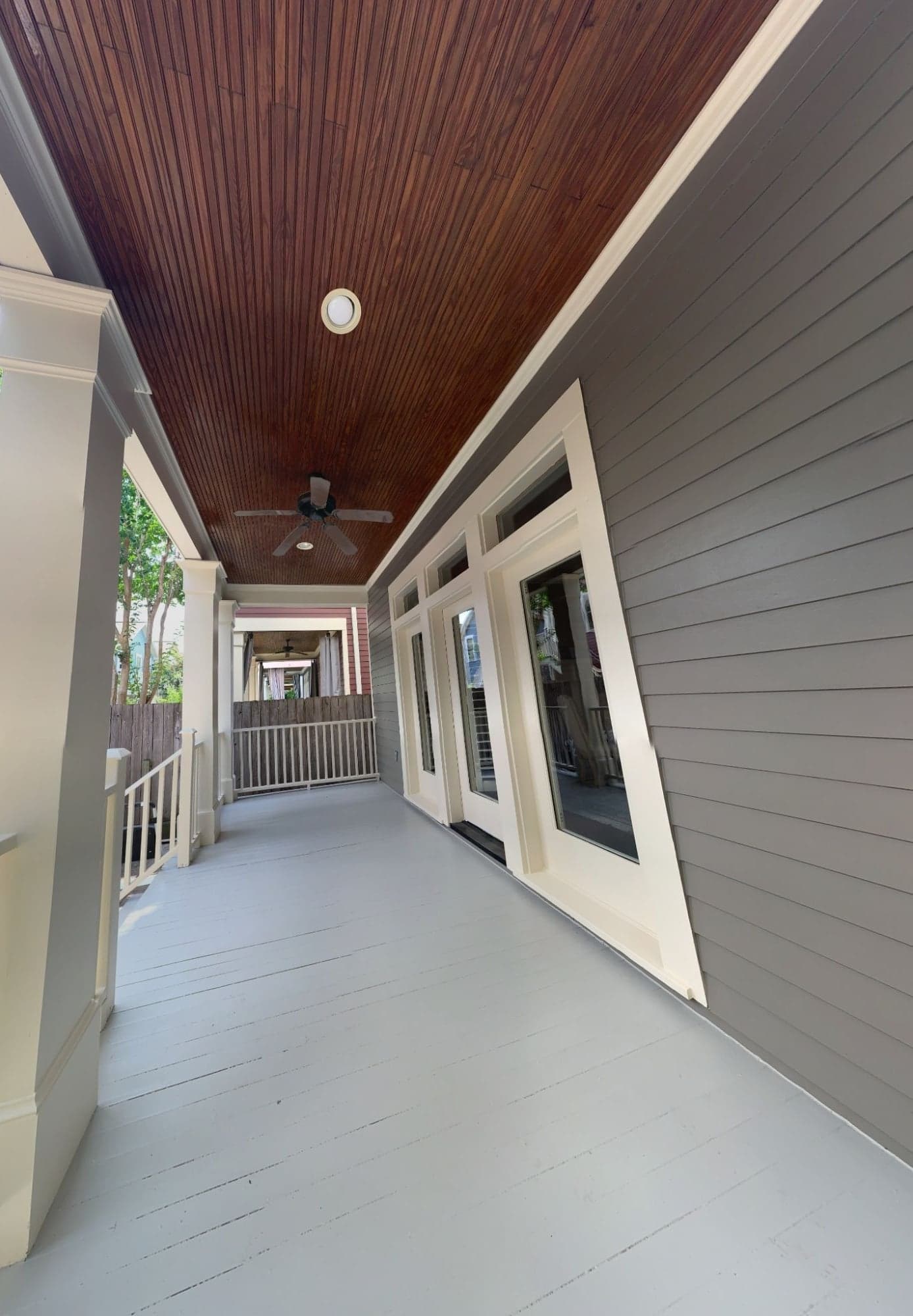 Long side porch with gray siding, cream trim and columns, a gray porch floor and a stained wood ceiling