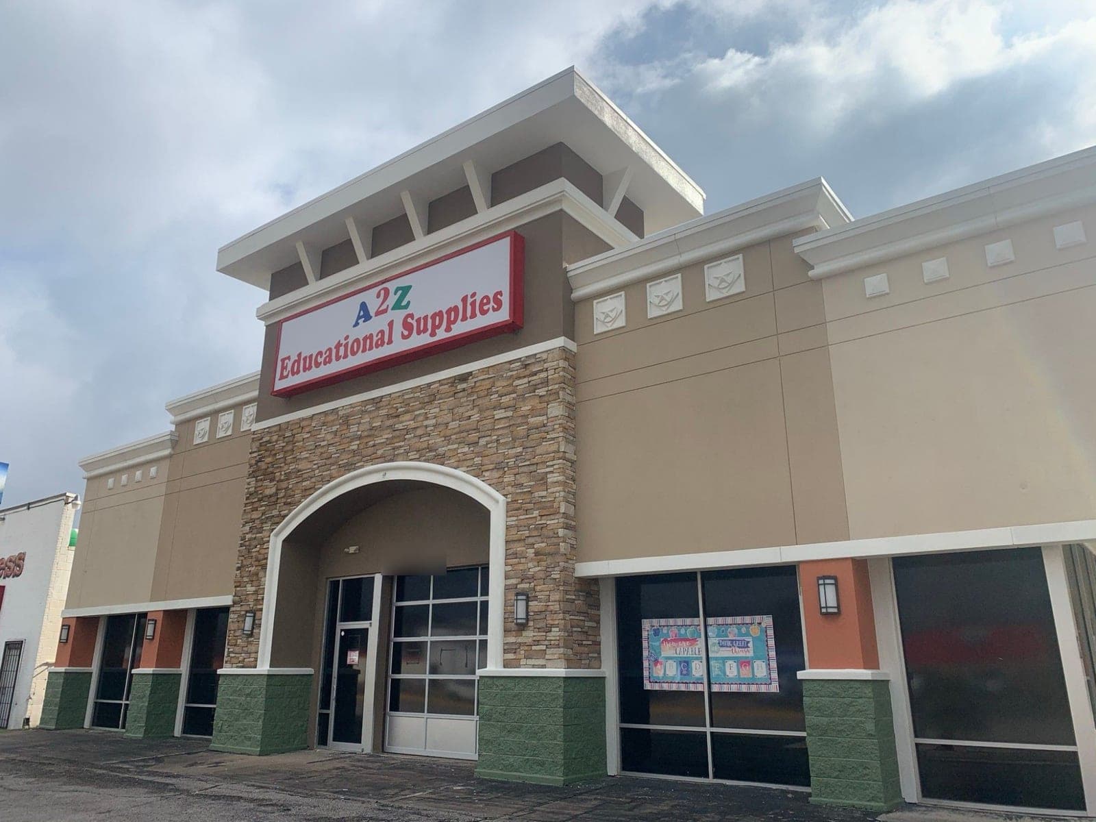 Retail center entry tower with tan stucco, white cornice and arch, stone veneer, orange columns and green block bases