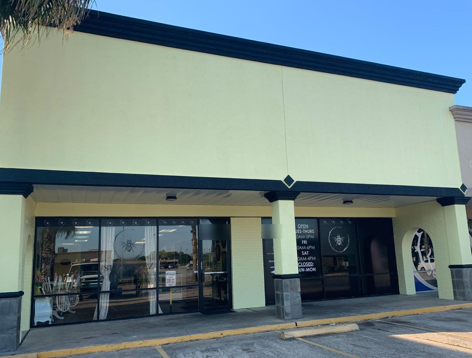 Storefront with soft yellow-green stucco and brick, black cornice and trim, and black column caps