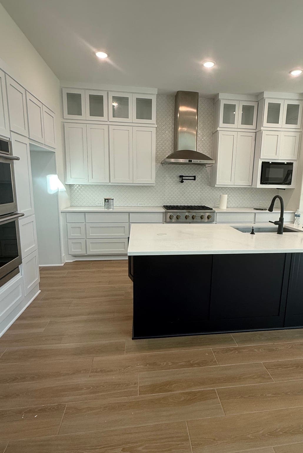 Katy kitchen with white shaker cabinets to the ceiling, glass-front uppers and a navy island with a white counter