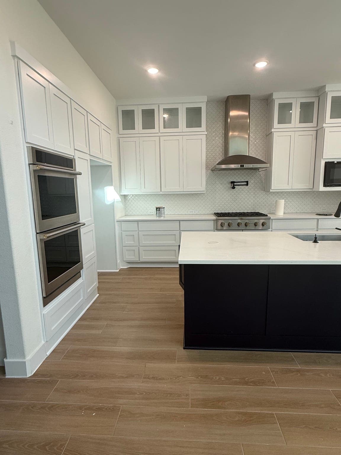 White cabinets around double wall ovens and stacked glass-front uppers beside the range hood