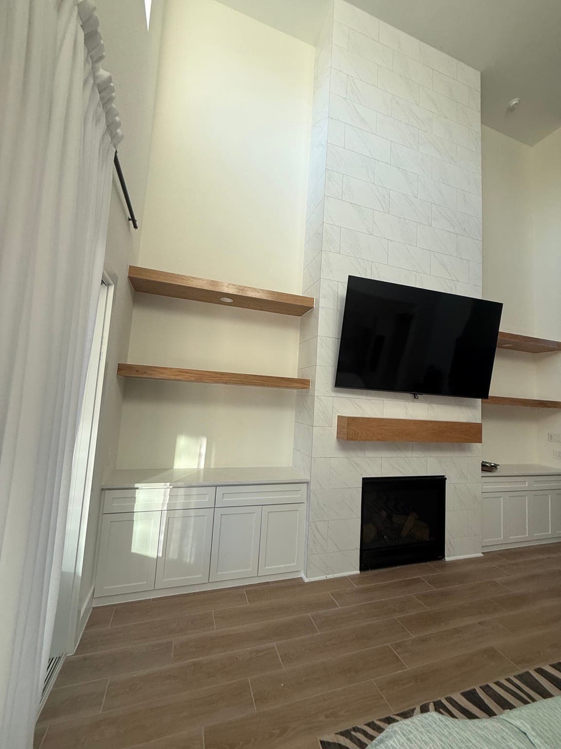 Living-room fireplace wall with white built-in cabinets and oak floating shelves on both sides