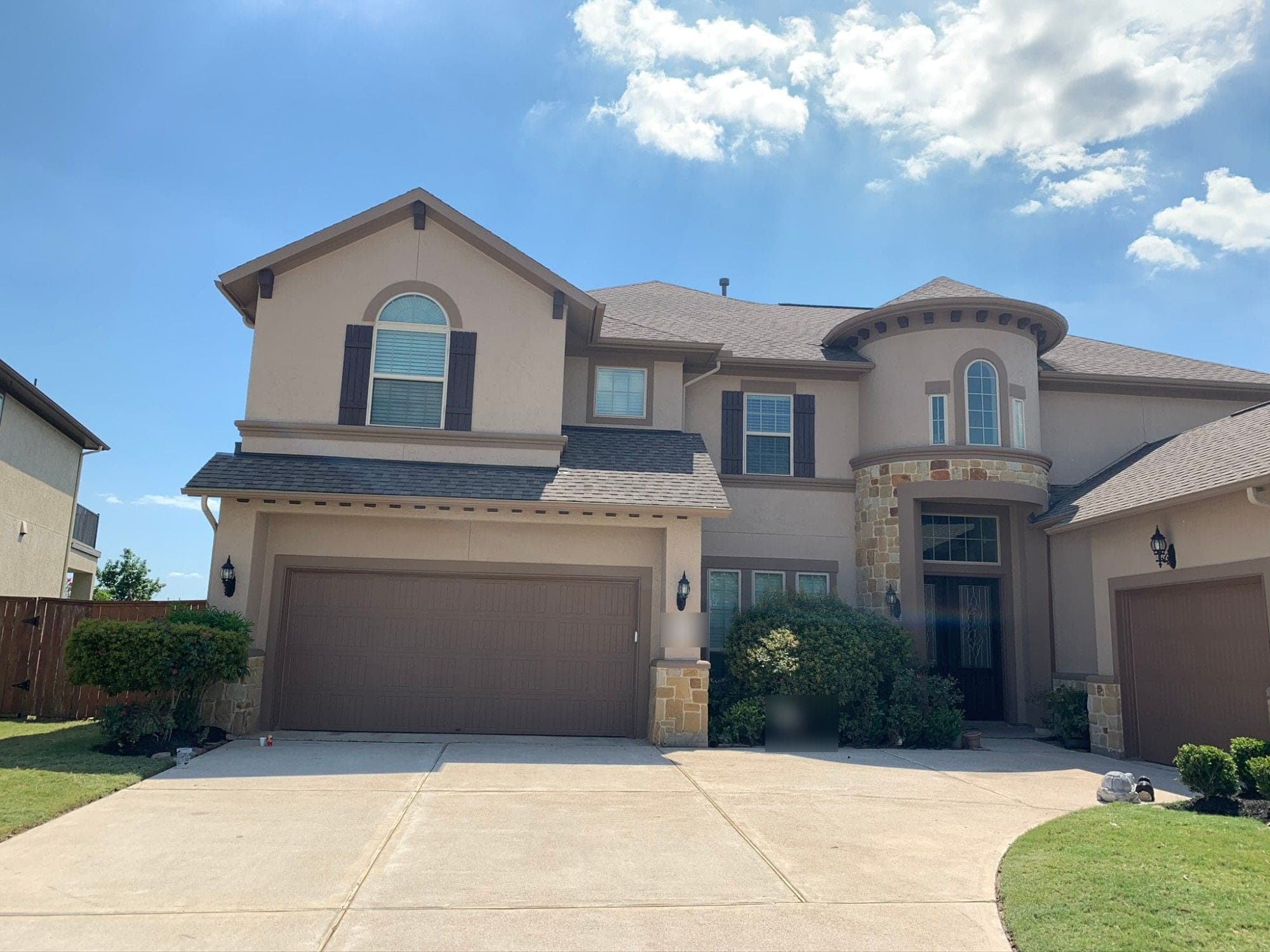 Katy two-story home with tan stucco walls, dark brown trim and shutters, and brown garage doors