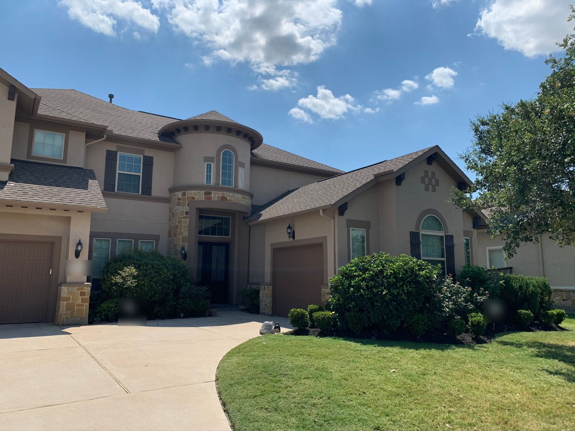 Tan stucco turret with stone base, dark trim around the arched windows and a brown single garage door