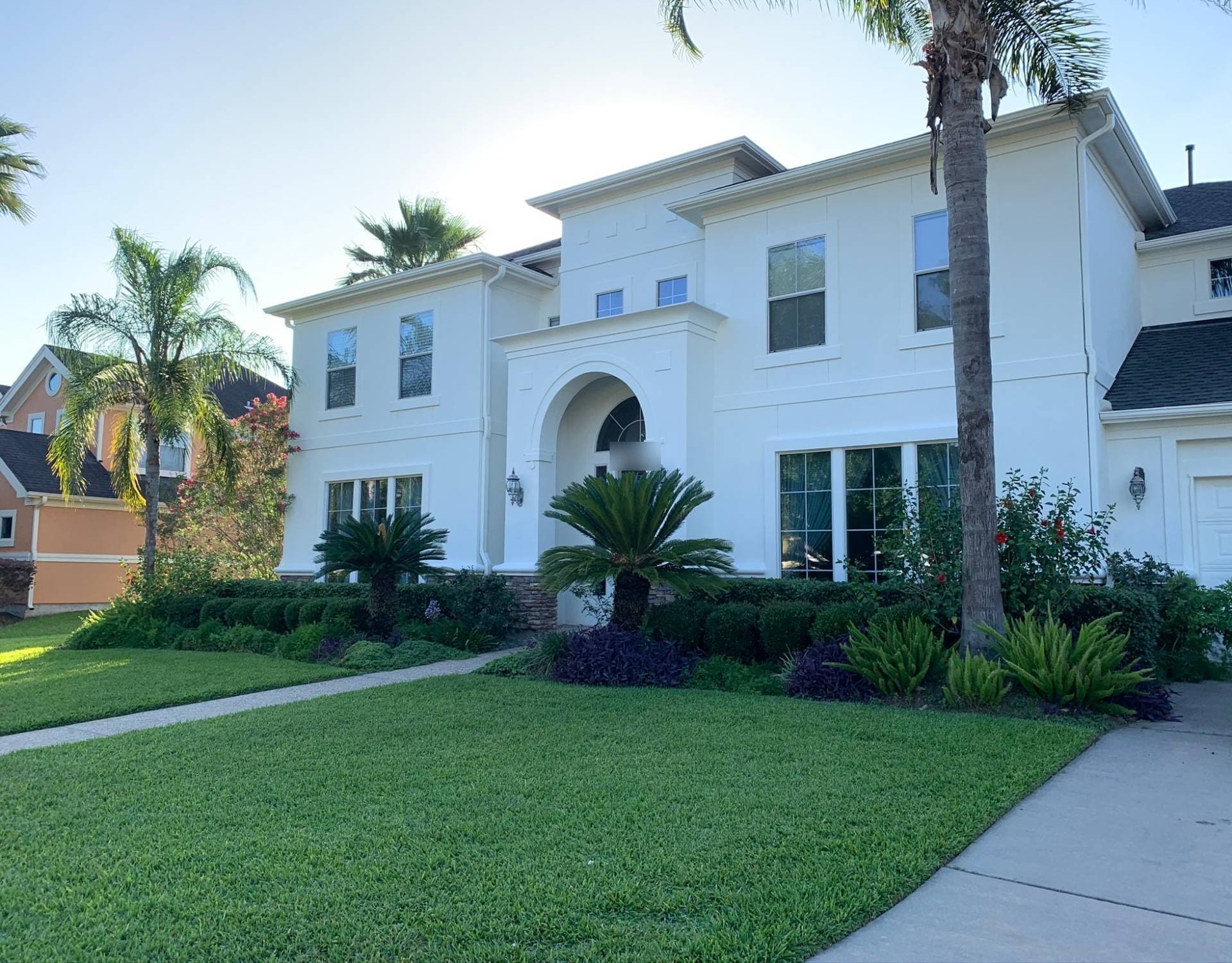 Katy two-story home with white stucco walls, an arched front entry and white trim behind palm trees
