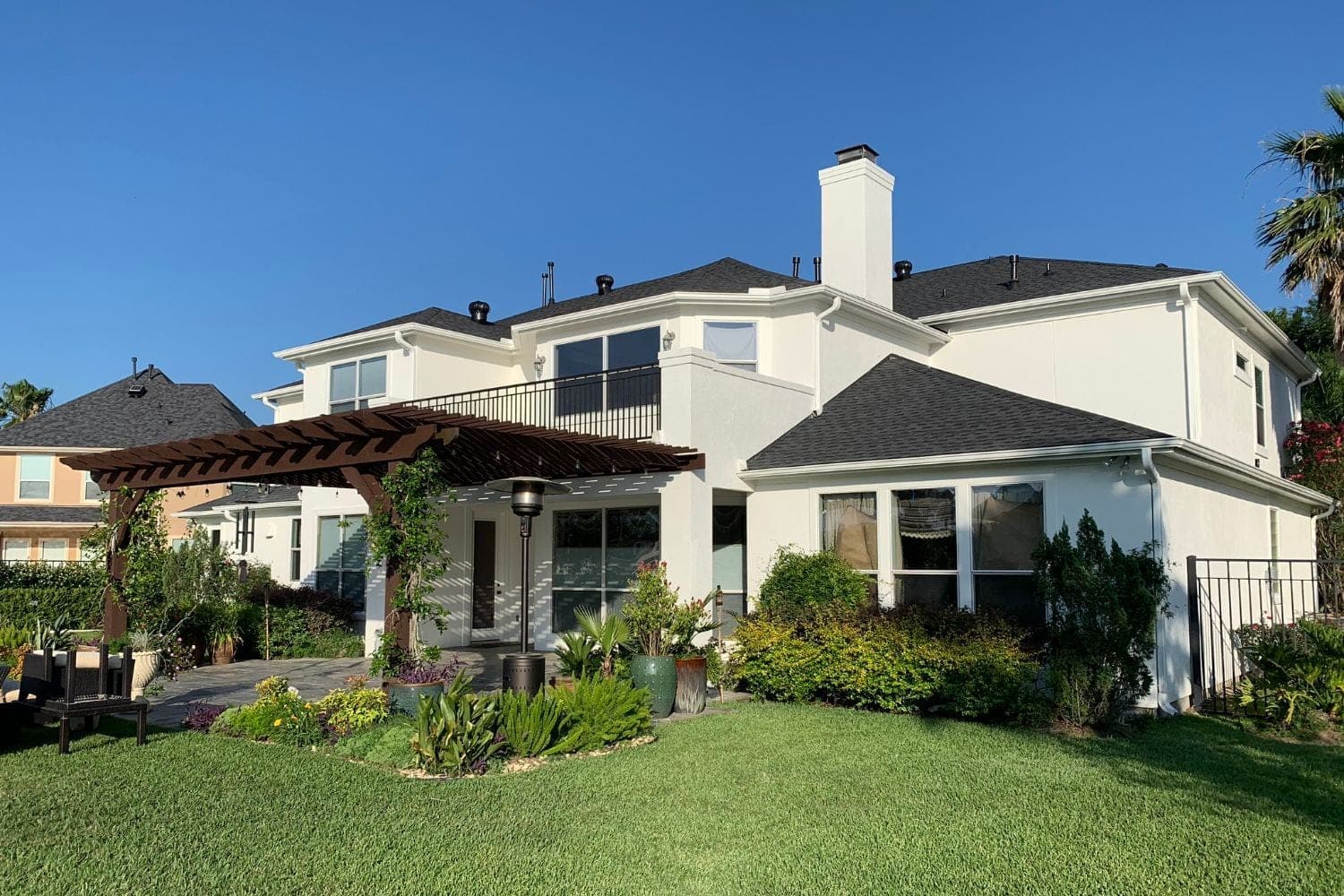 Back of the white stucco home with a second-floor balcony, covered patio and wood pergola