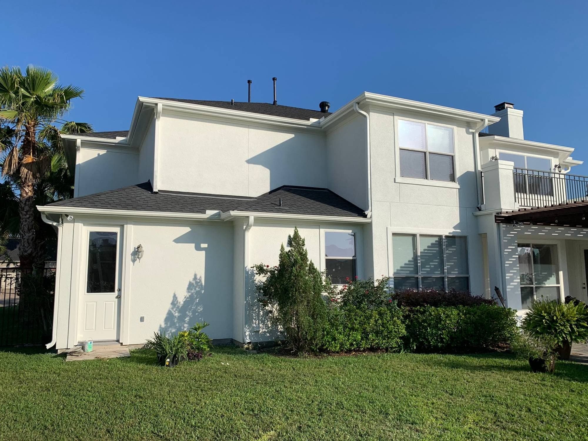 Side elevation of the white stucco home with white gutters, downspouts and a side door