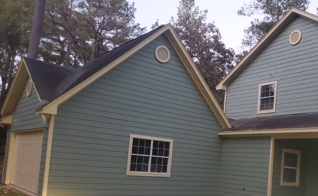 Garage wing and side gable with green lap siding, yellow trim and round gable vents