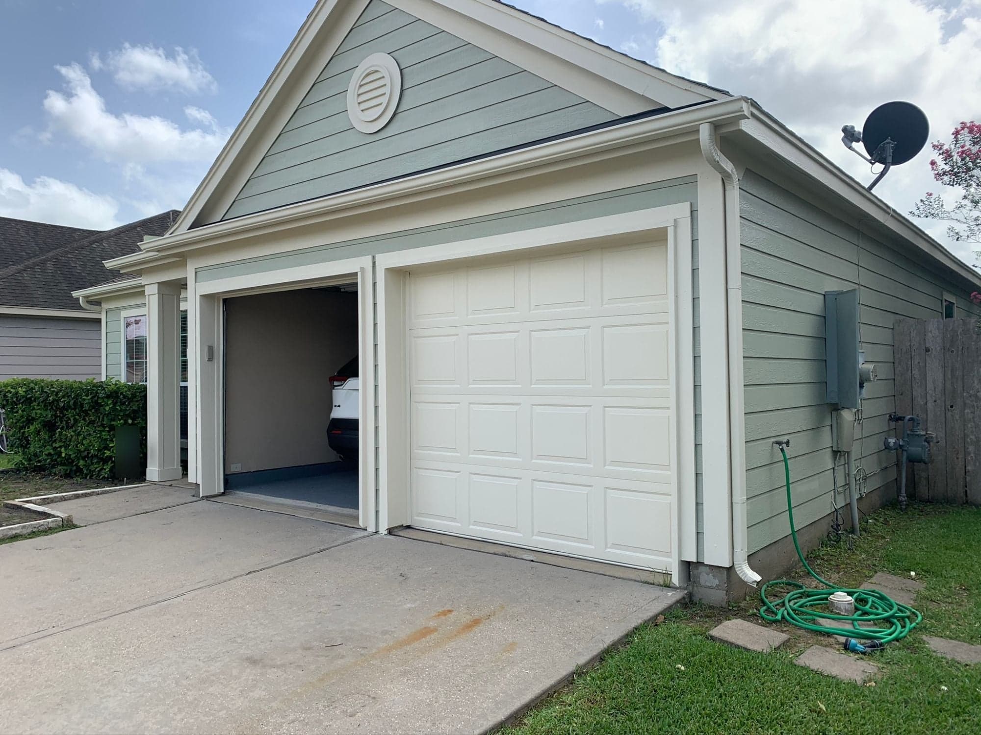 Garage elevation with sage-green siding, a round gable vent and cream trim and gutters