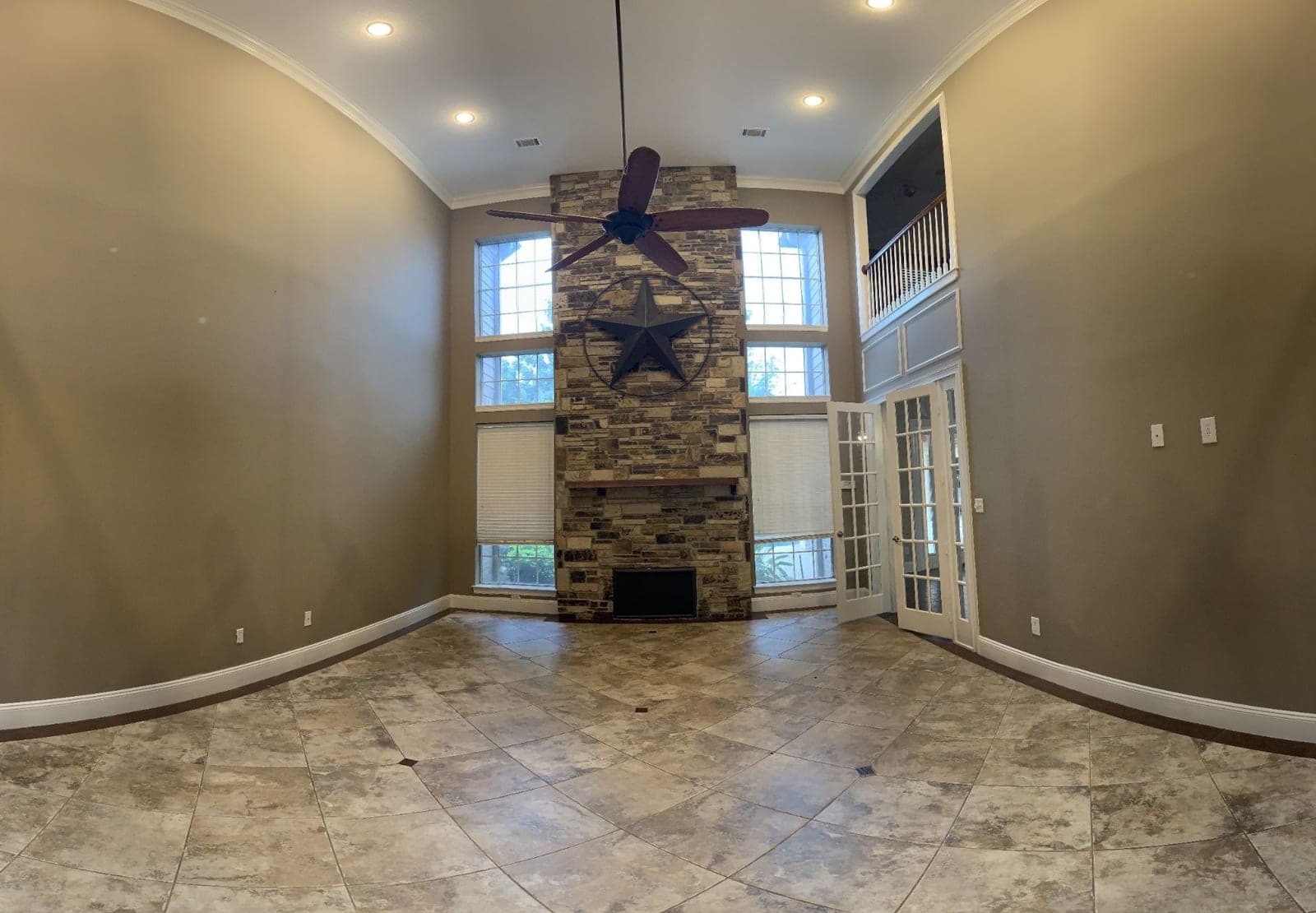 Two-story great room in Richmond with taupe walls, white crown molding and baseboards around a stone fireplace
