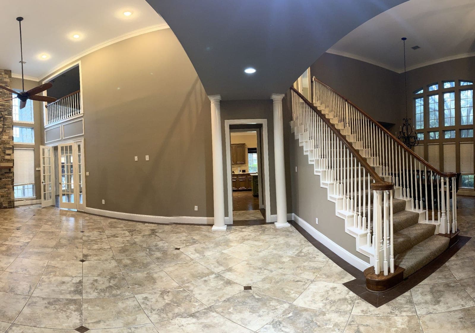 Wide view of the foyer with taupe walls, white columns, trim and stair skirt