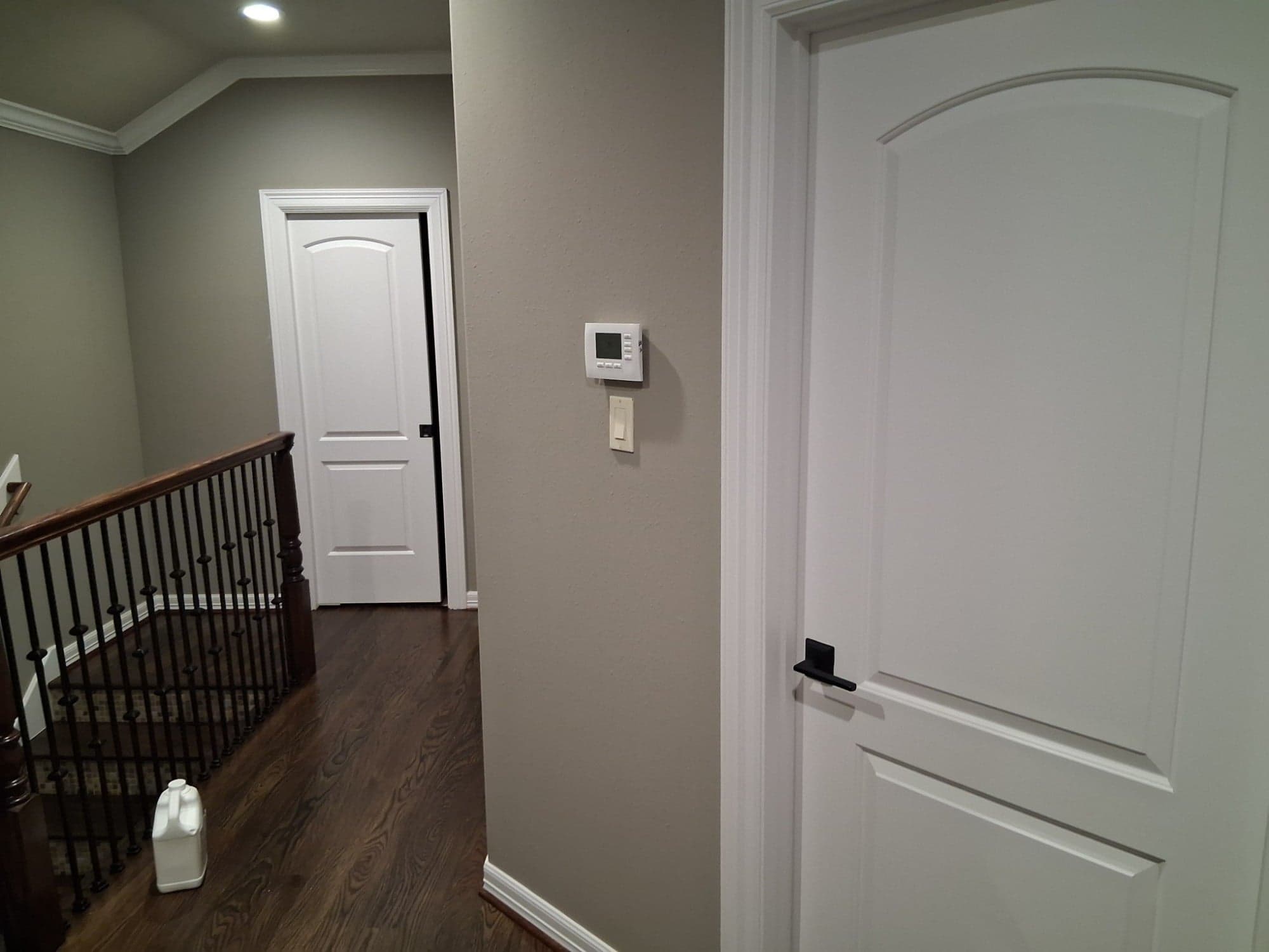 Upstairs landing with white two-panel doors and greige walls beside the stair railing