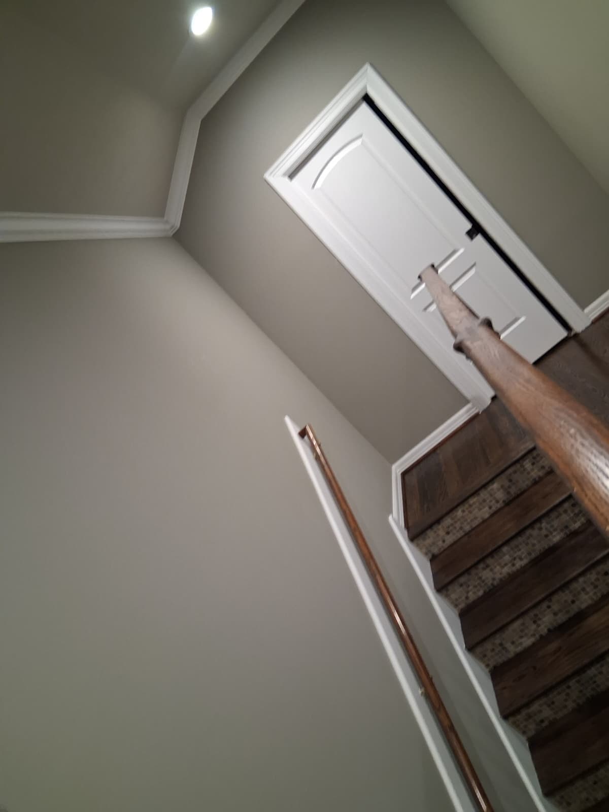 Two-story stairwell seen from below, with white crown molding and greige walls