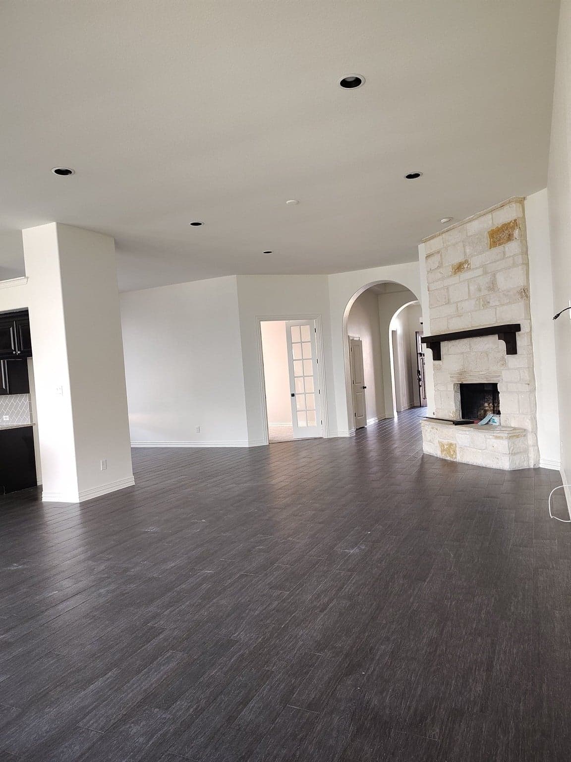Open living room with white walls and baseboards, arched openings and a stone fireplace