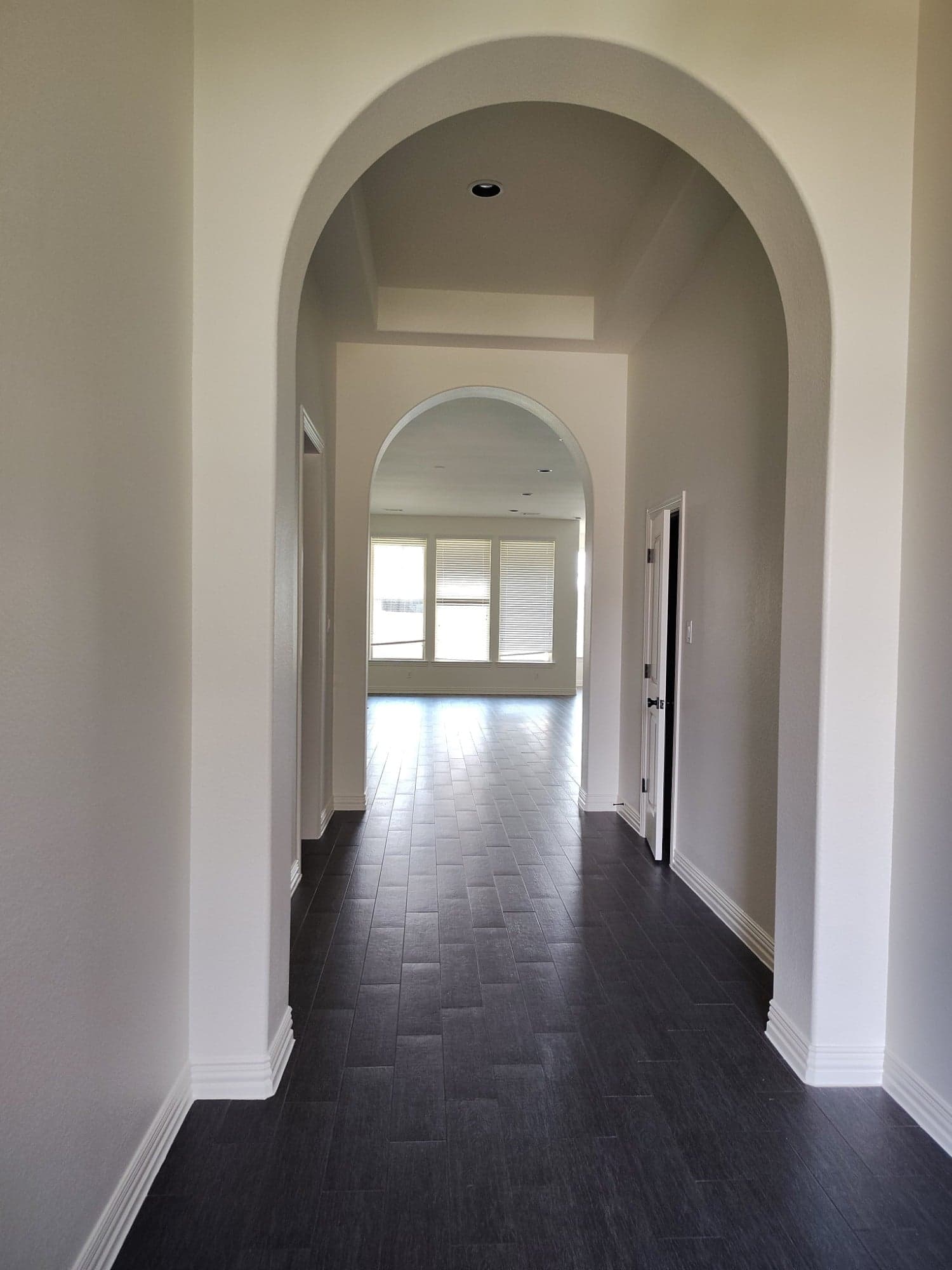 Hallway through two arched openings with white walls and baseboards