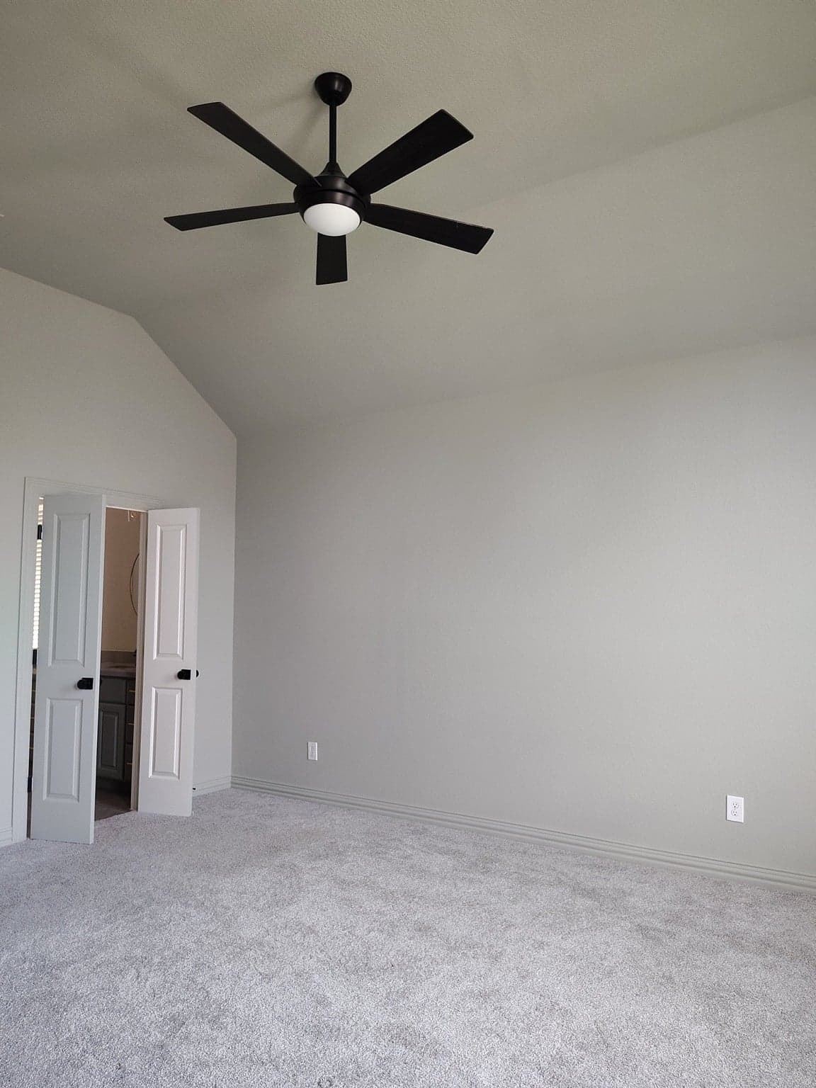 Bedroom with a vaulted ceiling, light gray walls and white double doors