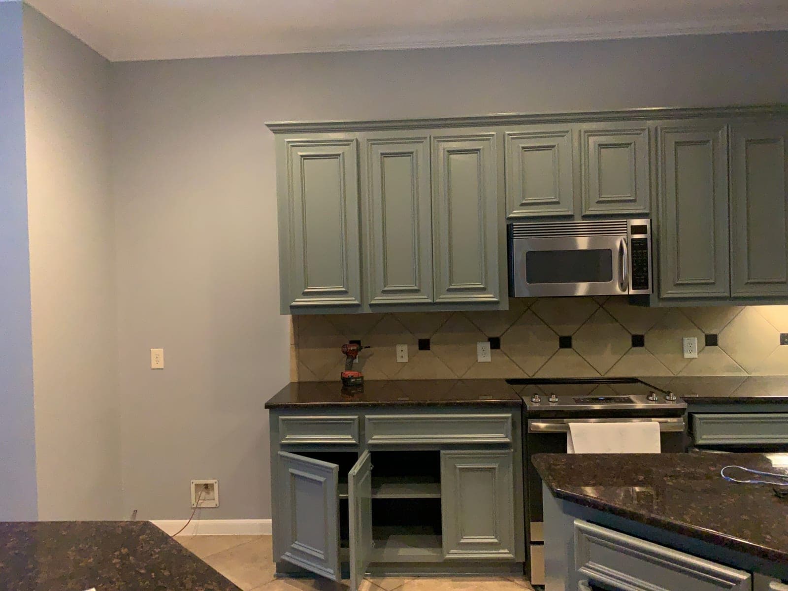 Sage green upper cabinets around the microwave, with crown molding painted to match