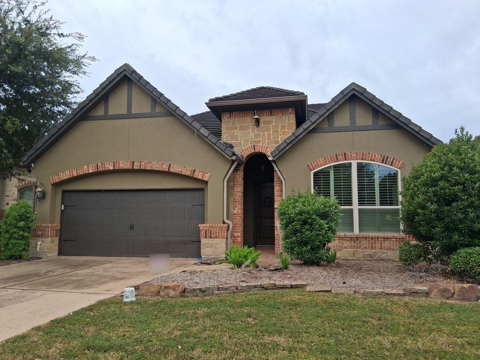 Sugar Land one-story home with olive-green stucco, dark brown gable boards and garage door, and brick arches