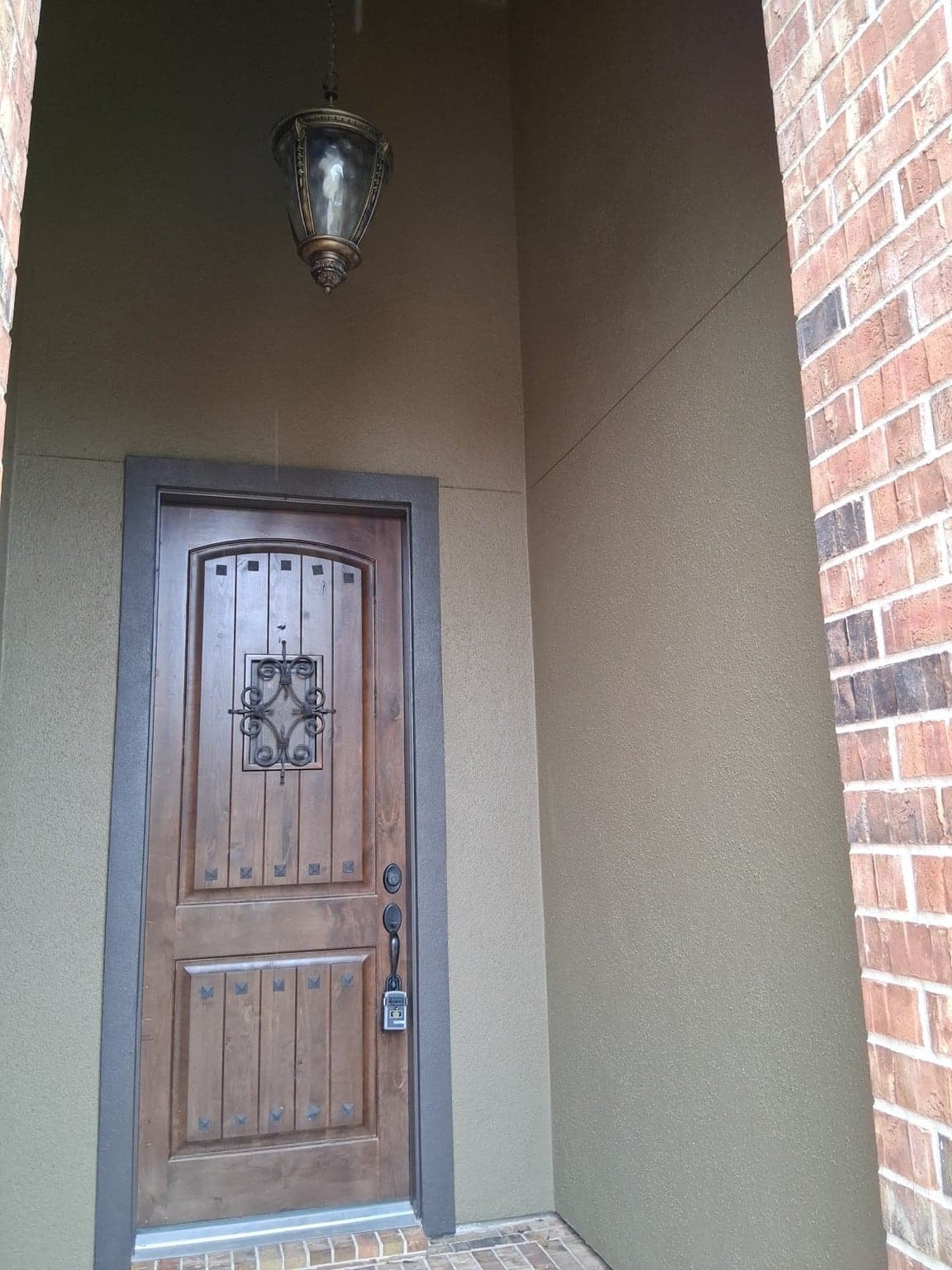 Recessed front entry with olive-green stucco walls and dark brown trim around a wood door