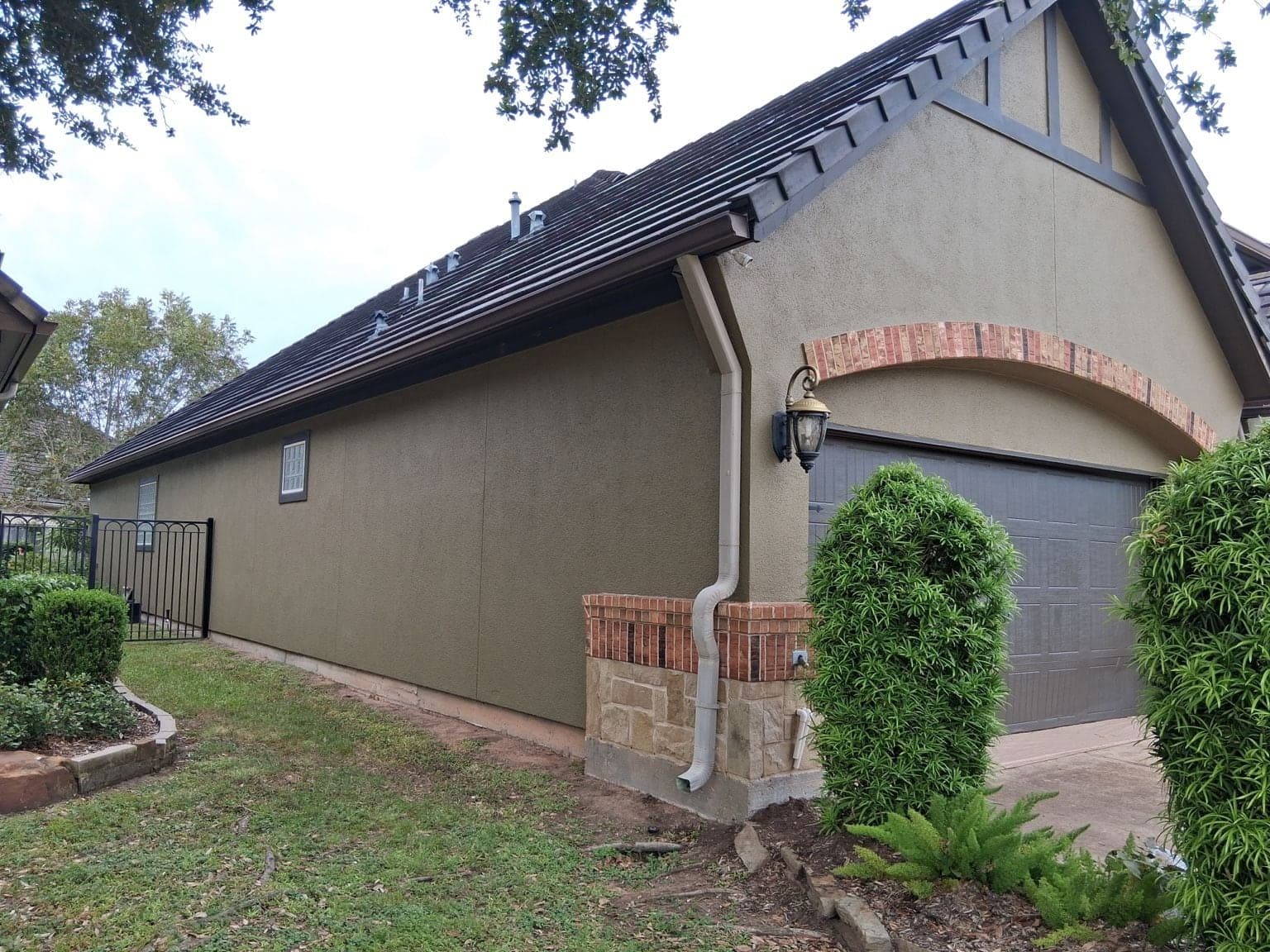 Long garage-side stucco wall in olive green with a dark brown gable and garage door