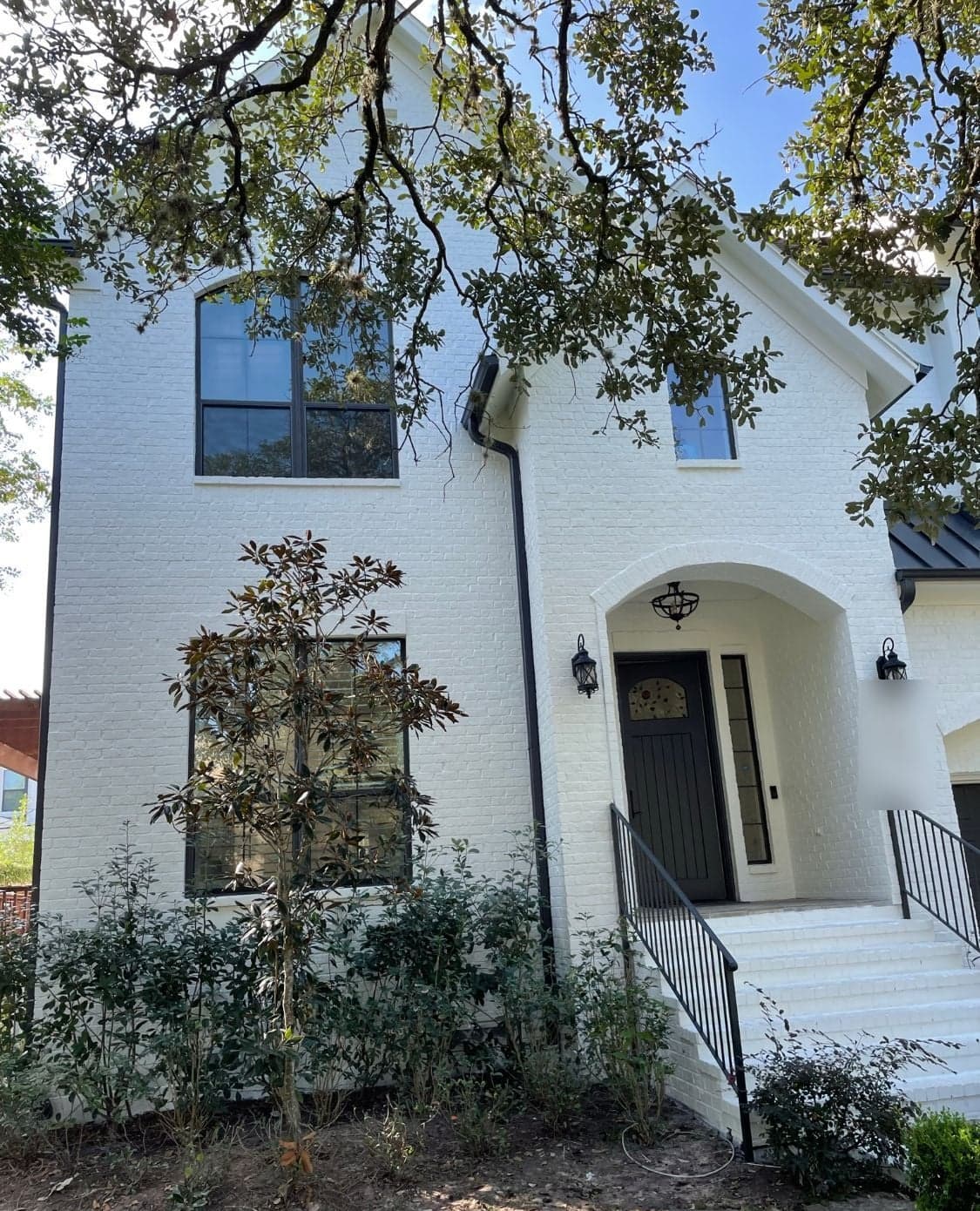 White painted brick front elevation with an arched entry, black front door and black window frames