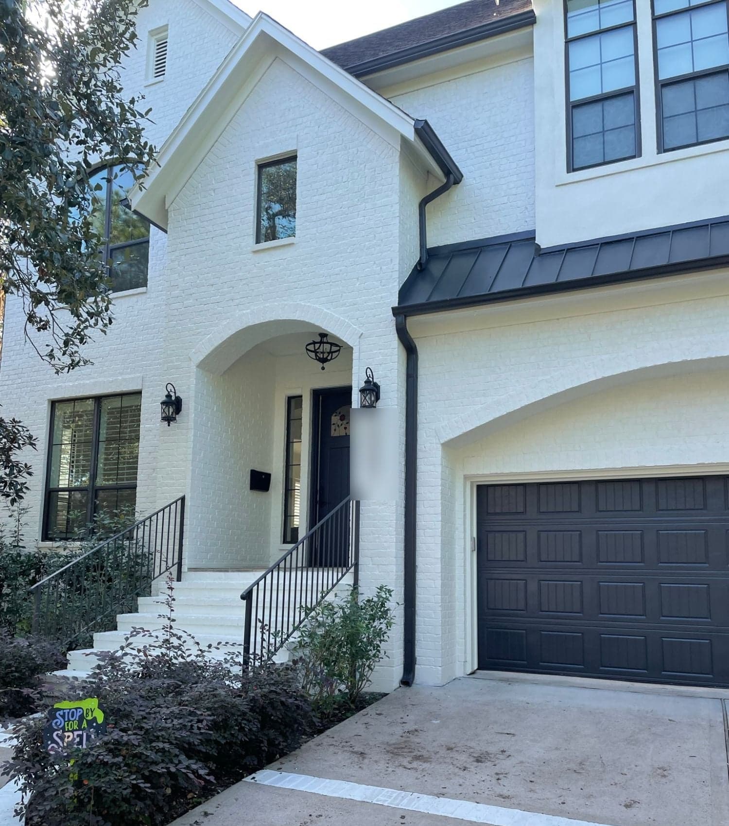 Painted brick entry steps, arched porch and garage with a black standing-seam metal roof accent