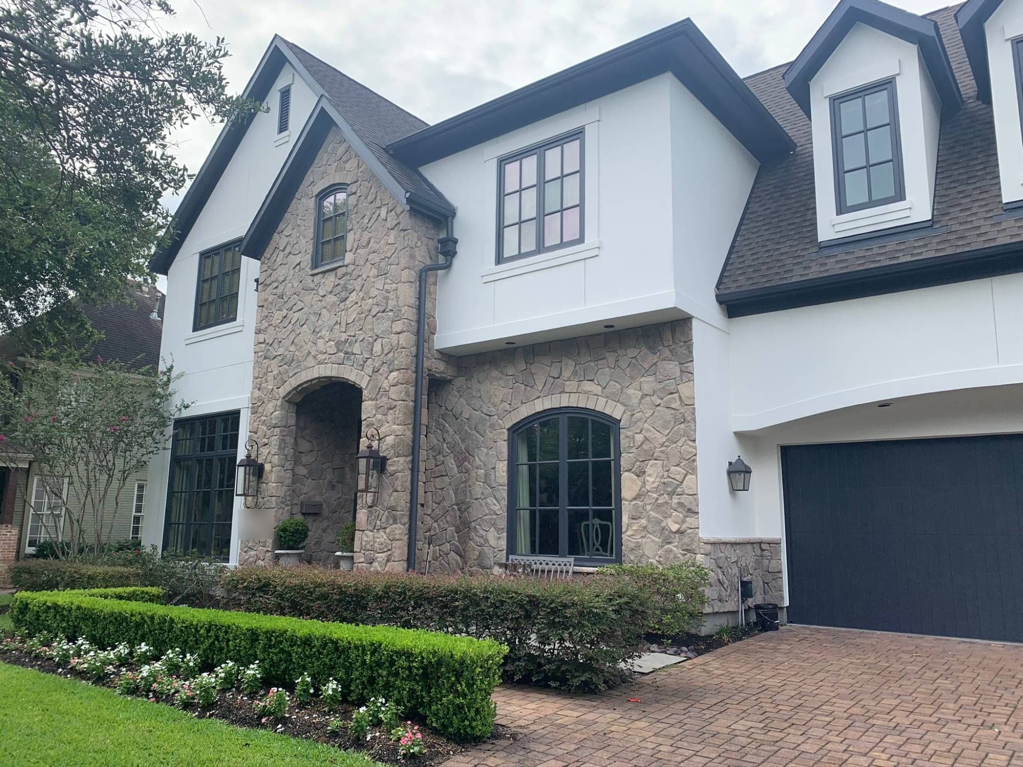 West University home with white painted stucco, a stone entry tower and dark window trim