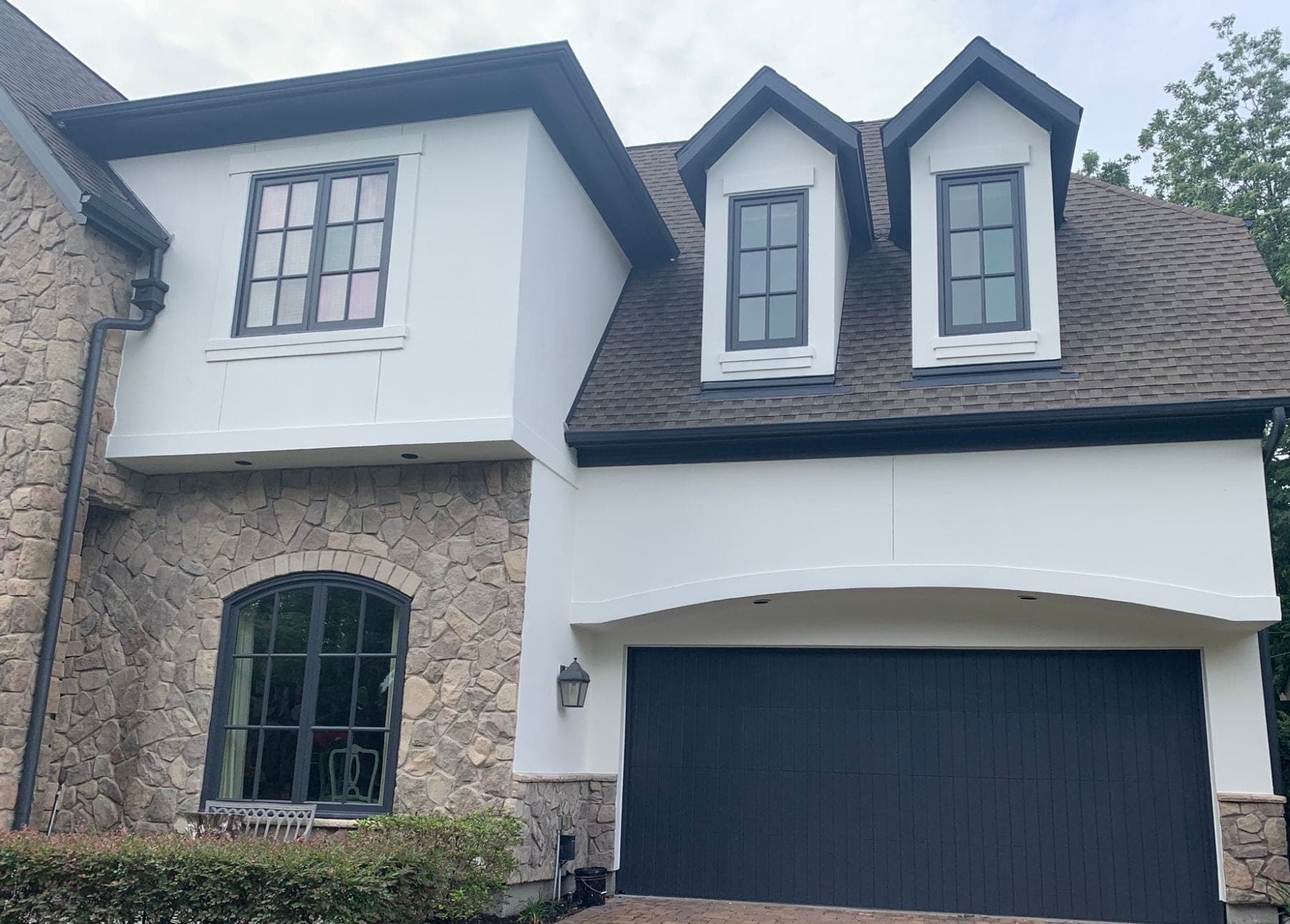 White stucco garage wing with an arched header, two dormers and a dark garage door