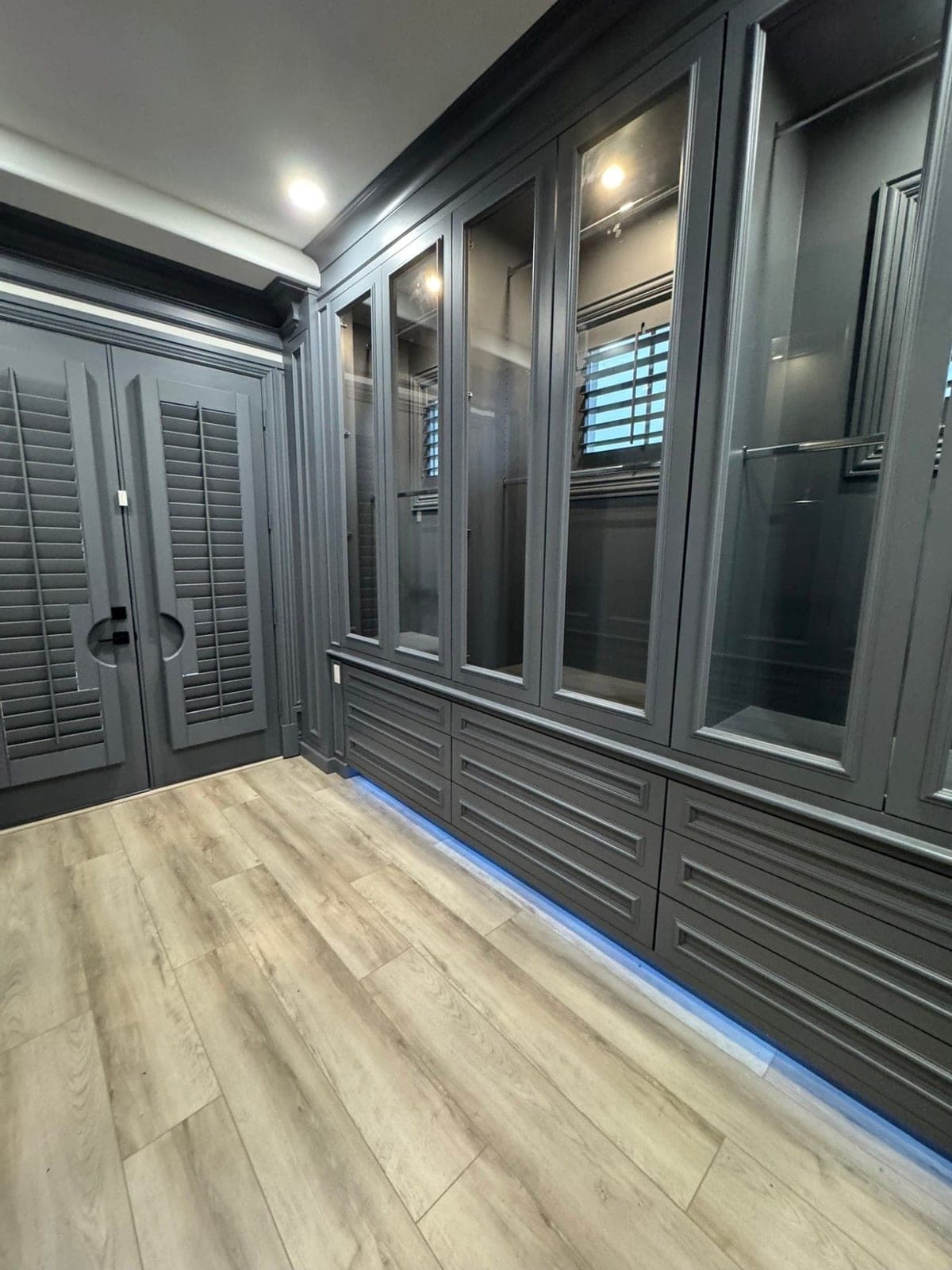 Walk-in closet with charcoal gray built-in cabinets, glass-front upper doors and raised-panel drawers