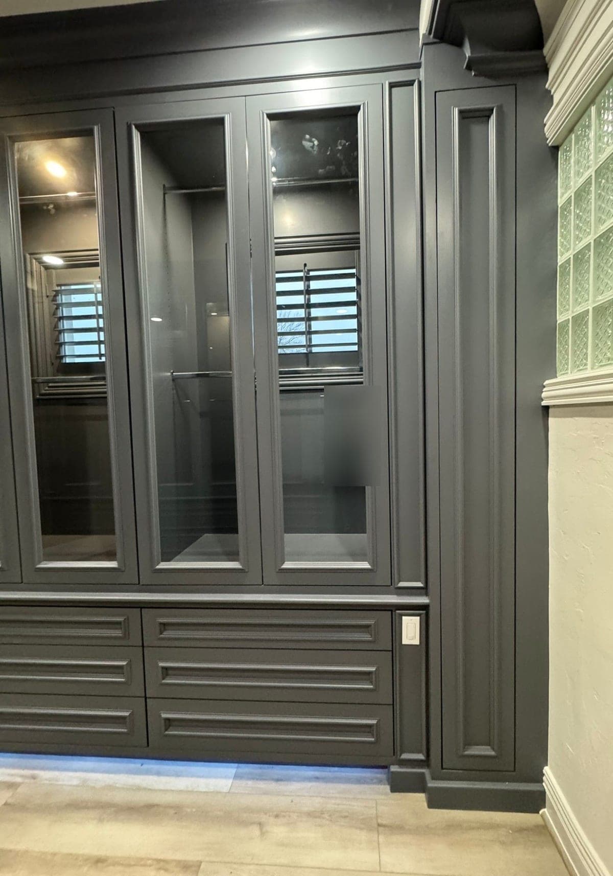 Charcoal gray glass-front closet cabinets with a raised-panel pilaster and three rows of drawers