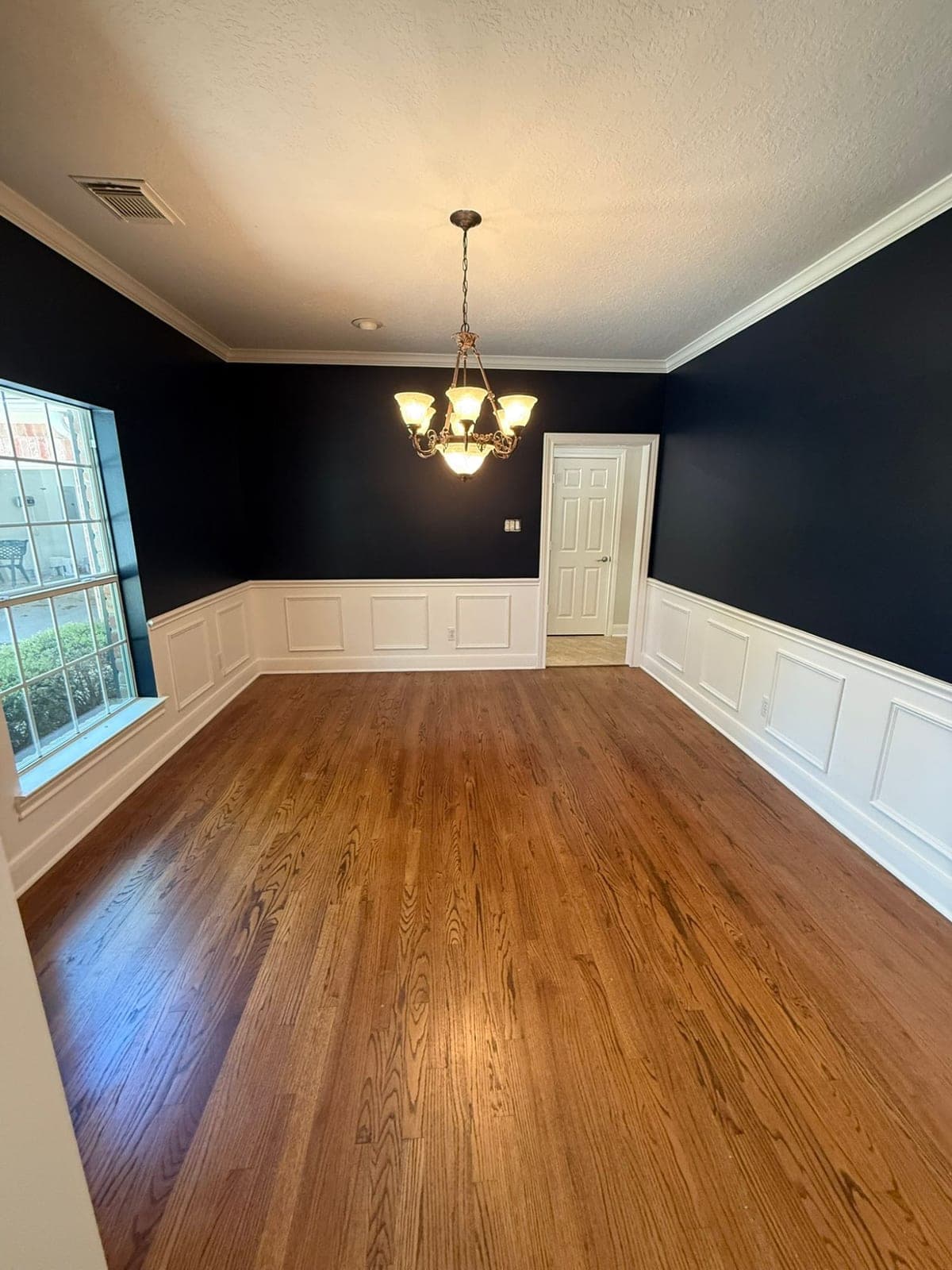 Weston Lakes dining room with navy walls above white panel wainscoting, white crown molding and a hardwood floor