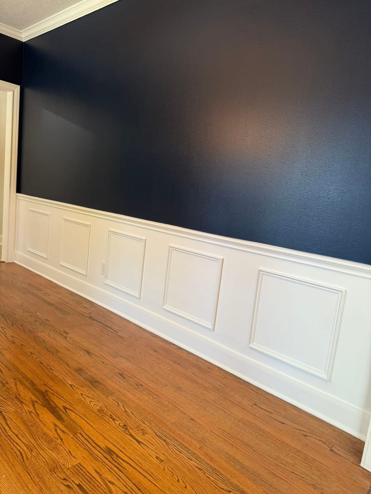 Close view of navy wall paint meeting white chair rail and picture-frame wainscot panels