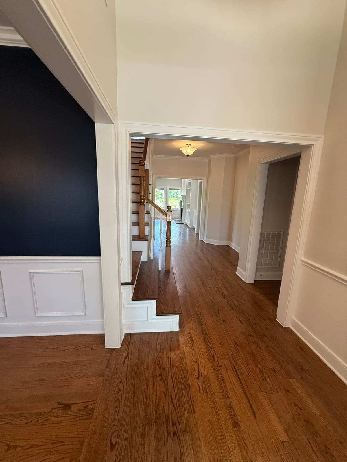 Foyer with a navy dining wall, white door casing and a light hallway leading past the staircase