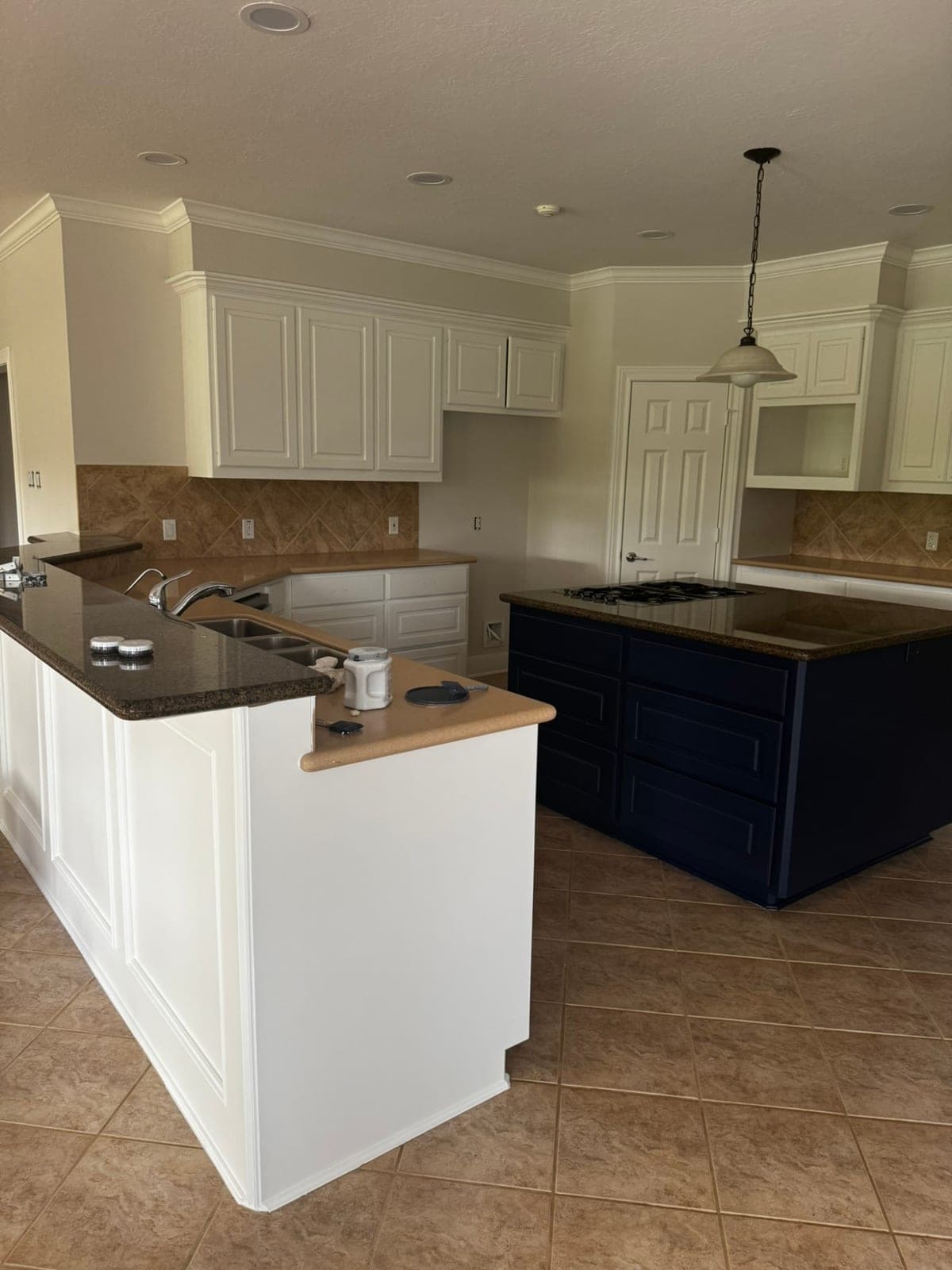 Kitchen with light walls, white crown molding and white cabinets beside a navy island