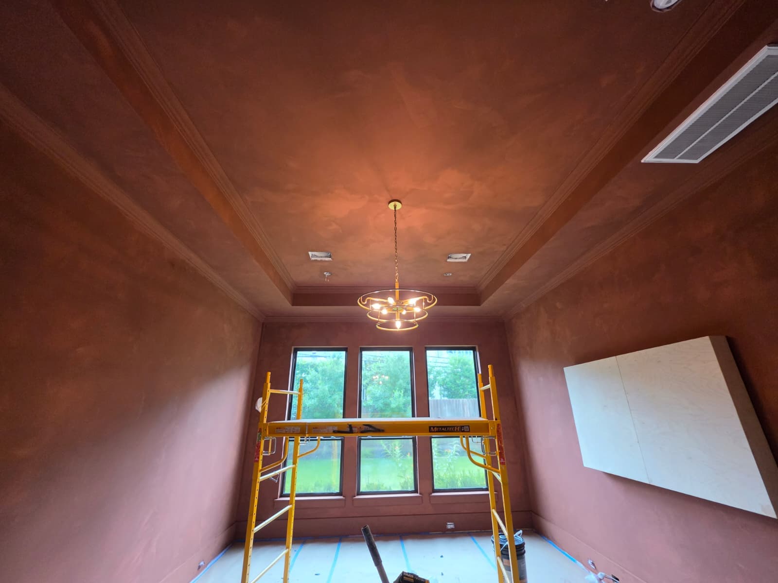 Terracotta Venetian plaster on a tray ceiling and walls of a Houston dining room, photographed mid-project with scaffolding in place